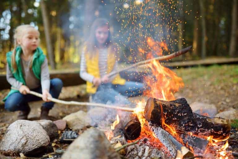 Cute little sisters roasting hotdogs on sticks at bonfire. Children having fun at camp fire. Camping with kids in Devon