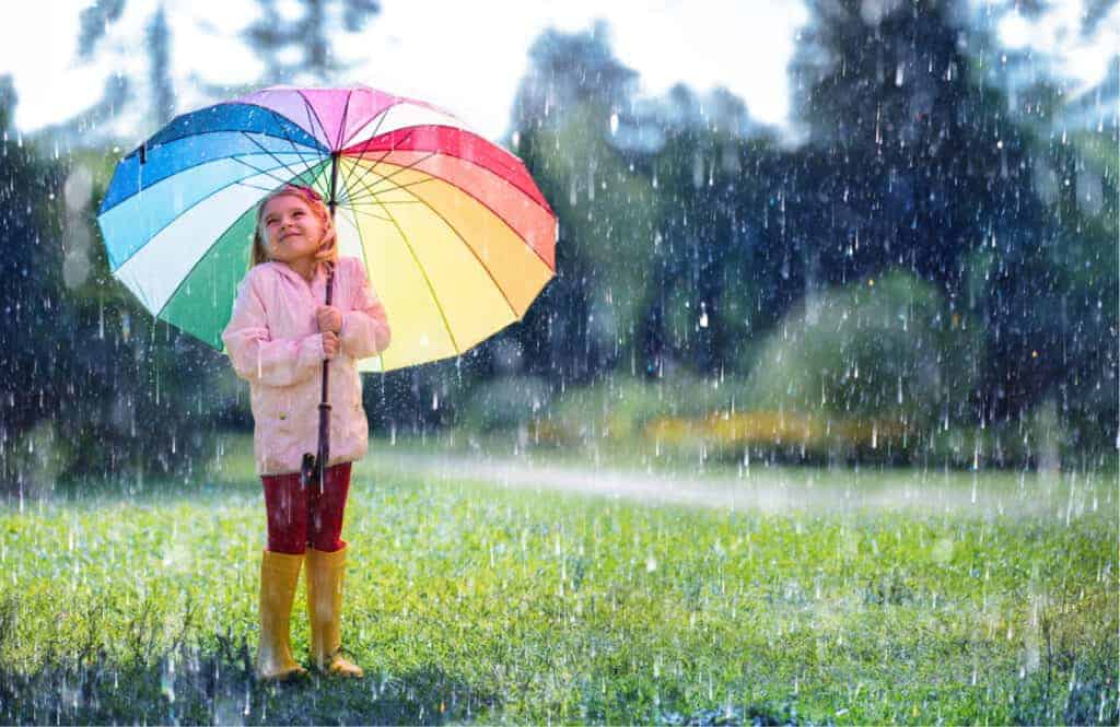 Child with rainbow umbrella standing in the rain