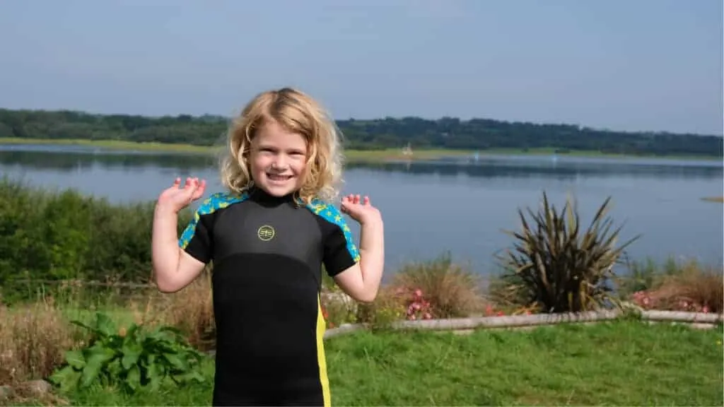 Girl in wetsuit standing in front of lake