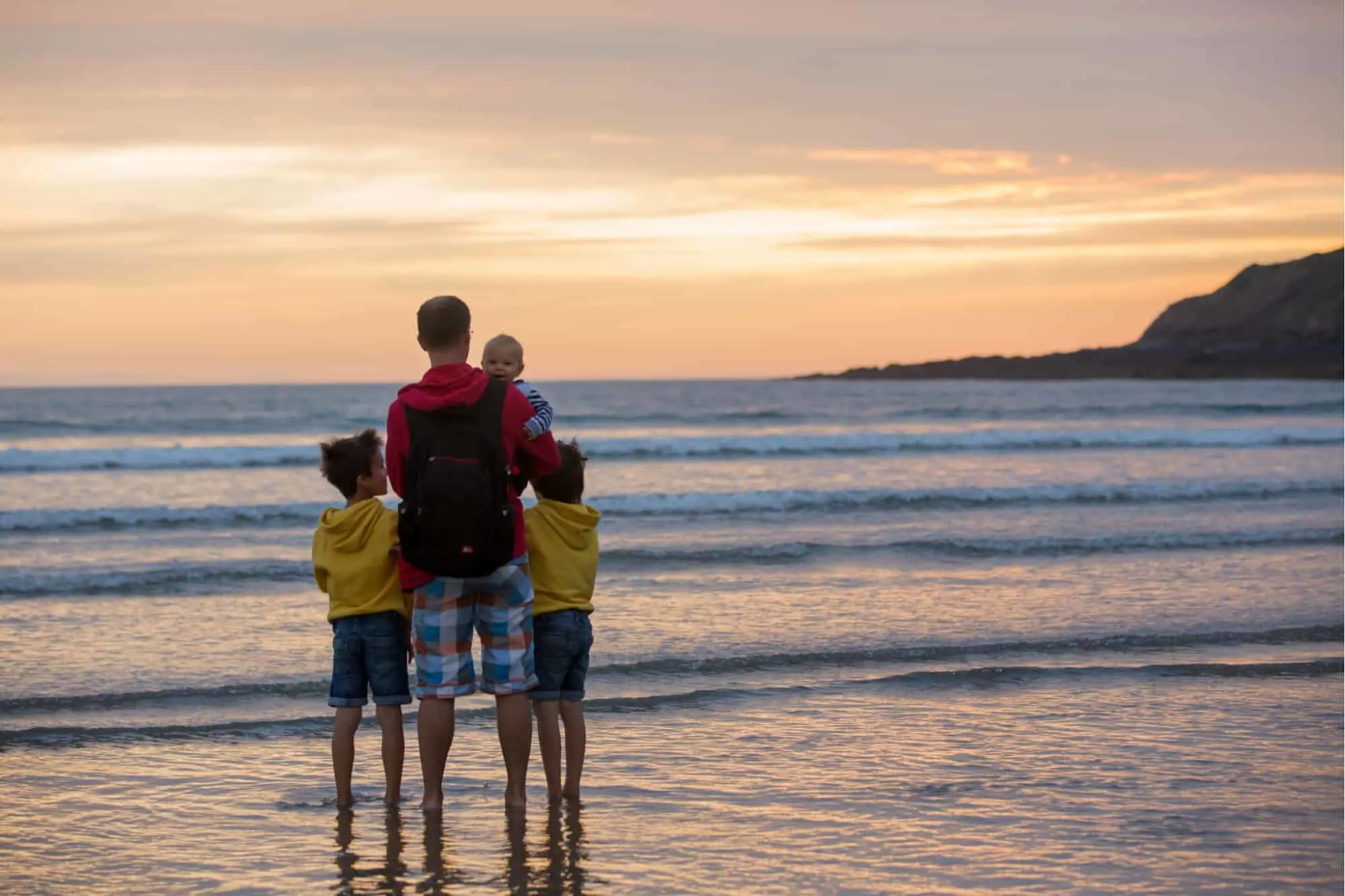 Young father with his beautiful children, enjoying the sunset over the ocean on a low tide in Devon, England