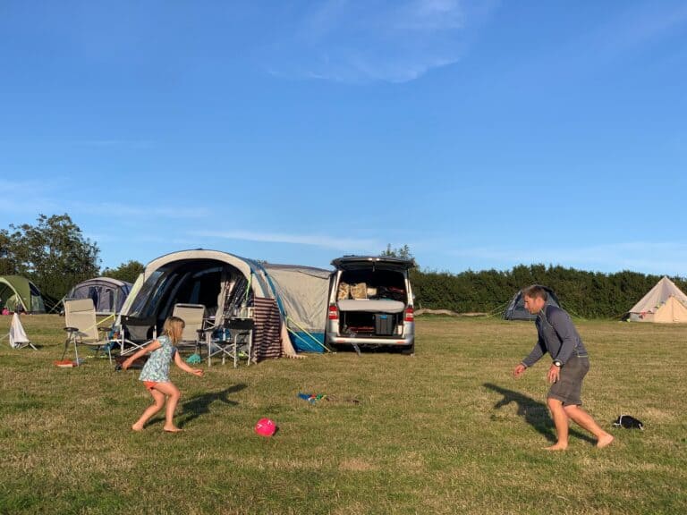 Family playing football in front of camper van and awning