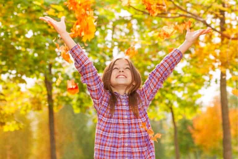 Girl throws orange leaves in the air in October autumn park