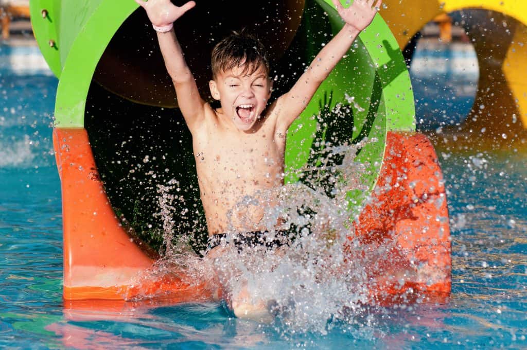 Boy goes into pool after going down water slide during summer