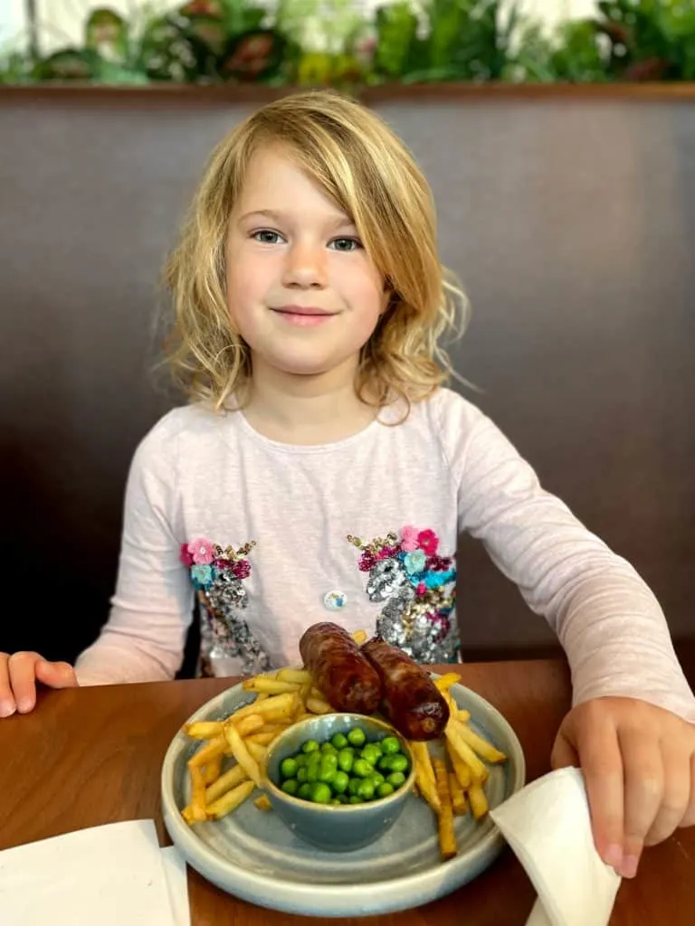 Child with plate of sausage, chips and peas