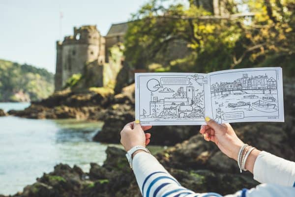 Hands holding up page with illustration of Dartmouth Castle with the same view in the background