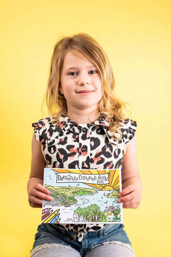 Child holding the Dartmouth Colouring Book for Kids with bright yellow background
