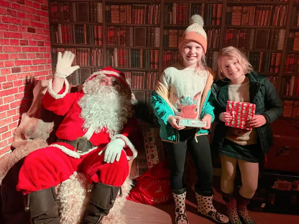 Two children holding presents next to waving Santa at Pennywell Farm