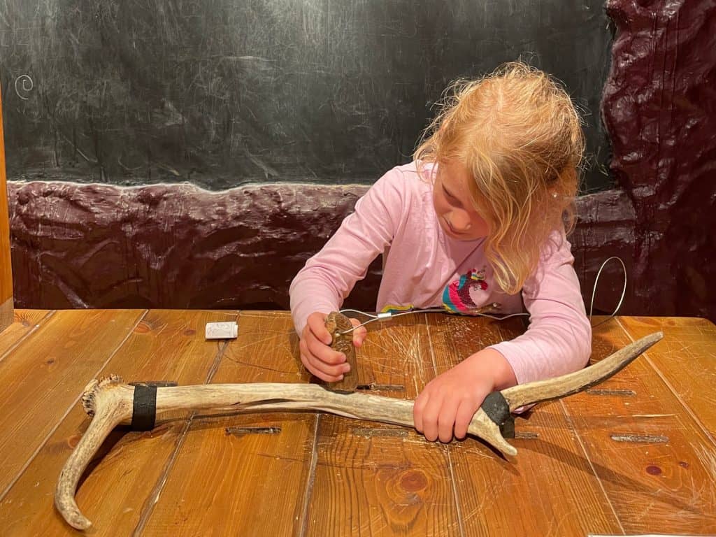 Child using a pre-historic tool to carve a animal antler