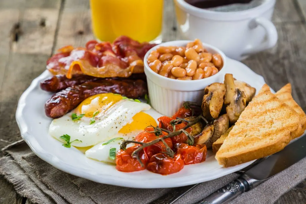 Full english breakfast - eggs, bacon, beans, toast, coffee and juice, rustic wood background