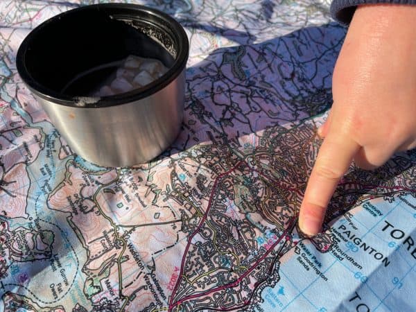 Child's hand pointing to map on picnic blanket with cup of hot chocolate to the side