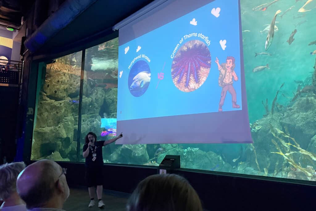 Projector screen with a family-focused presentation happening in front of the Eddystone Reef tank during the school holidays
