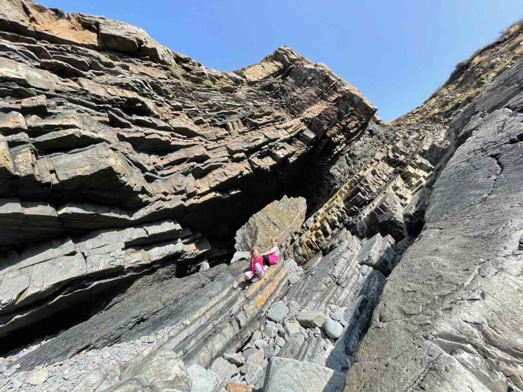 Children sat under folds of rock at Hartland Quay