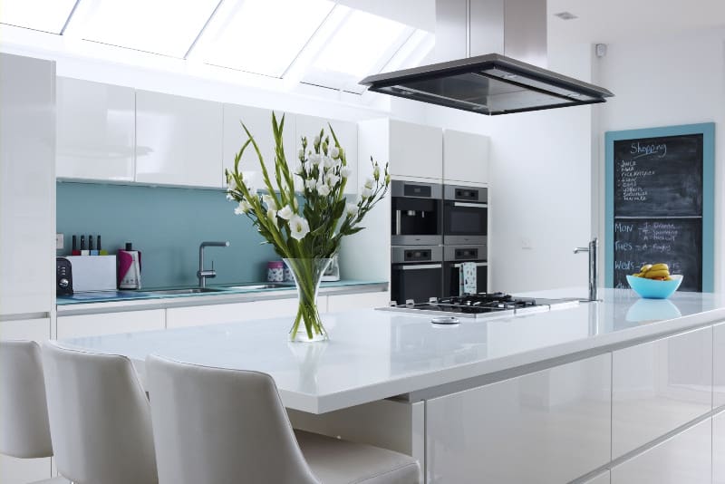 Open plan white kitchen with large vase of flowers