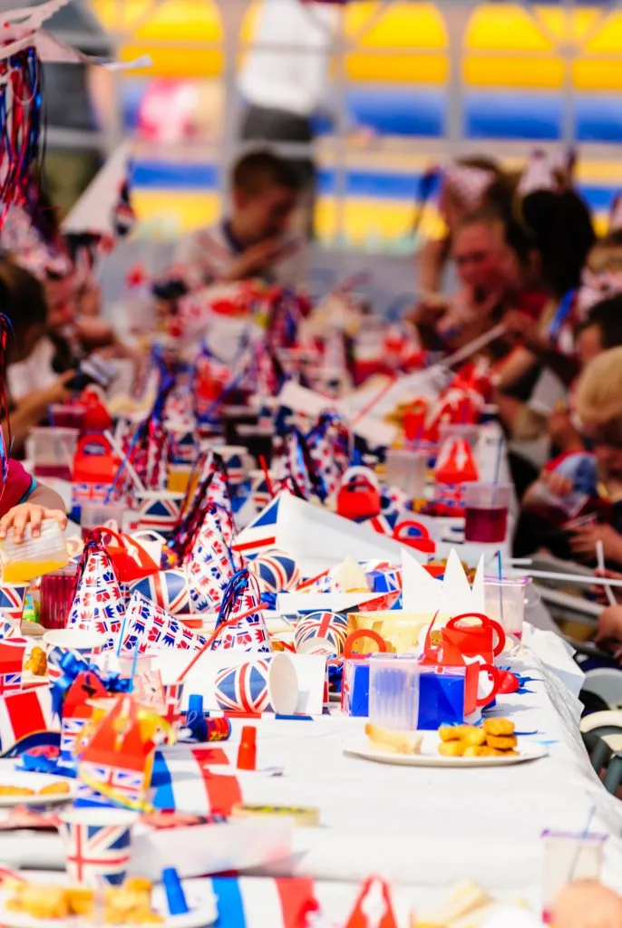 Children sit at long tables with red, white and blue party accessories at a Royal event street party