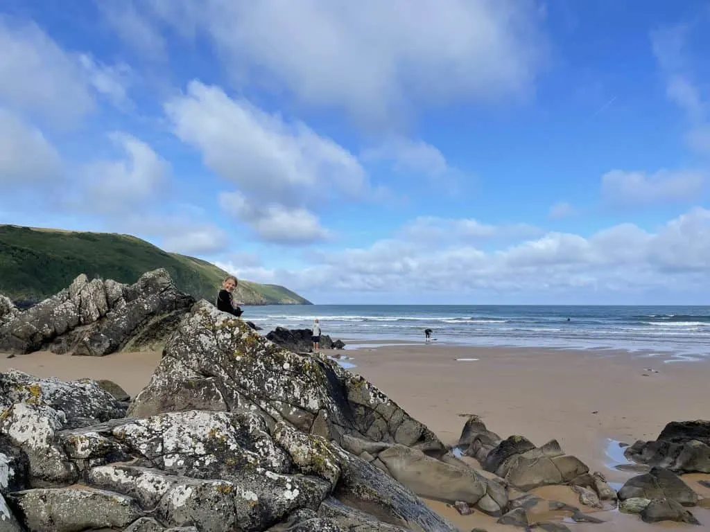 View Putsborough Sands beach with child sat on rocks