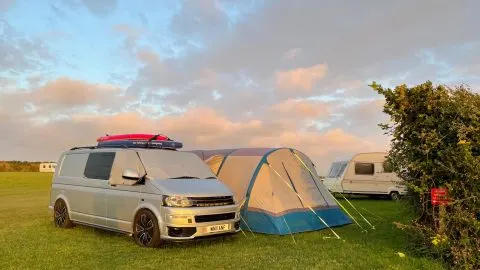 Camper van and awning on grass pitch beside hedge