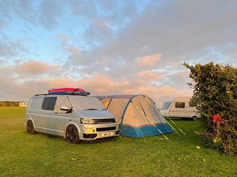 Camper van and awning on grass pitch beside hedge