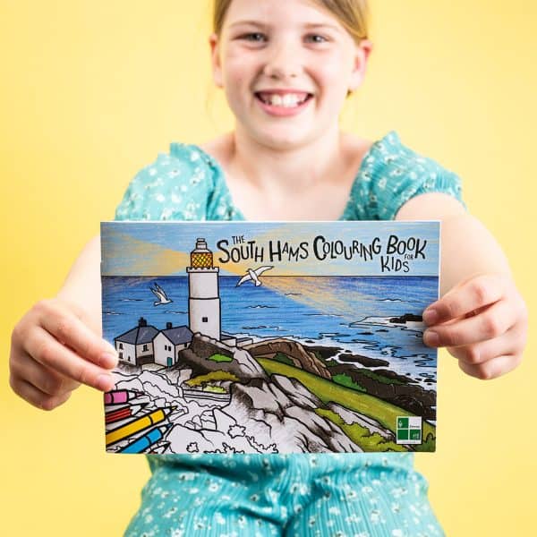 Child holding up cover of the South Hams Colouring Book for Kids while sat against a bright yellow background