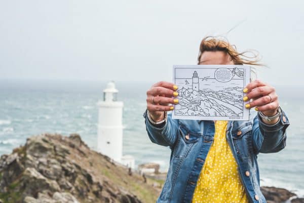 Colouring book page with an illustration of the Start Point Lighthouse being held up in front of the same view