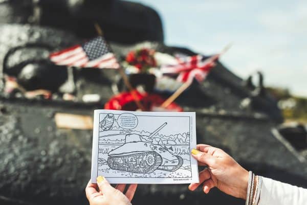 Colouring book page with an illustration of Slapton Sands WWII Tank being held up in front of the same view