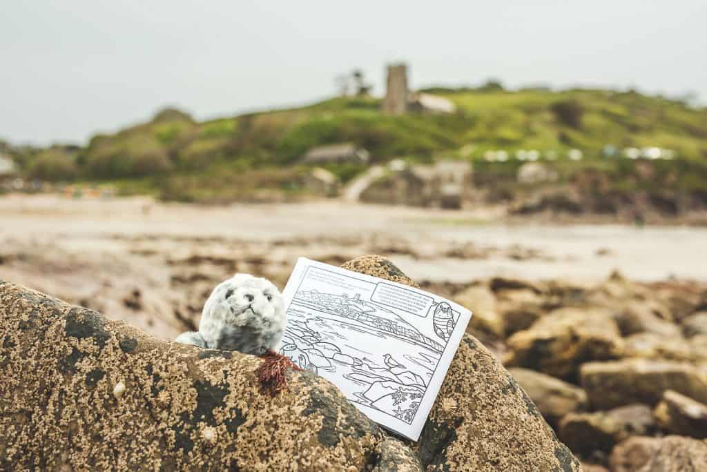 Colouring book page with an illustration of Wembury Beach in front of the same view