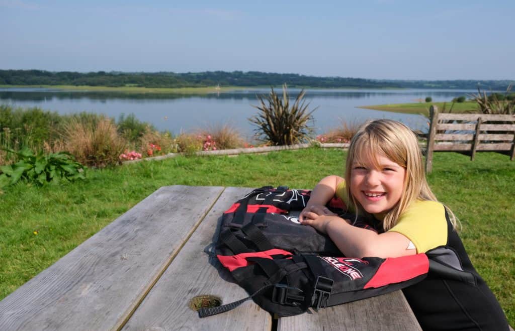 Child in wetsuit sat on picnic table in front of Roadford Lake