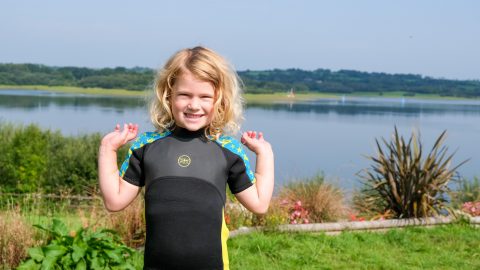 Child wearing wet suit stood in front of lake view