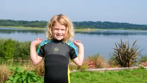 Child wearing wet suit stood in front of lake view