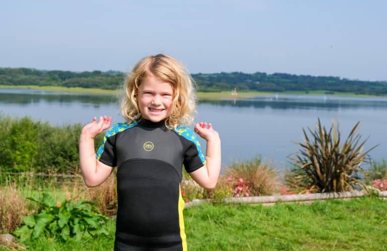 Child wearing wet suit stood in front of lake view