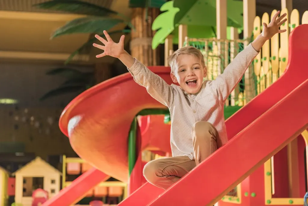 happy little boy smiling at camera while playing on slide in soft play centre