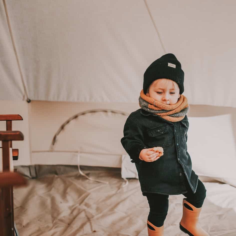 Young child wrapped up in coat, hat scarf and welly boots dances in a canvas tent