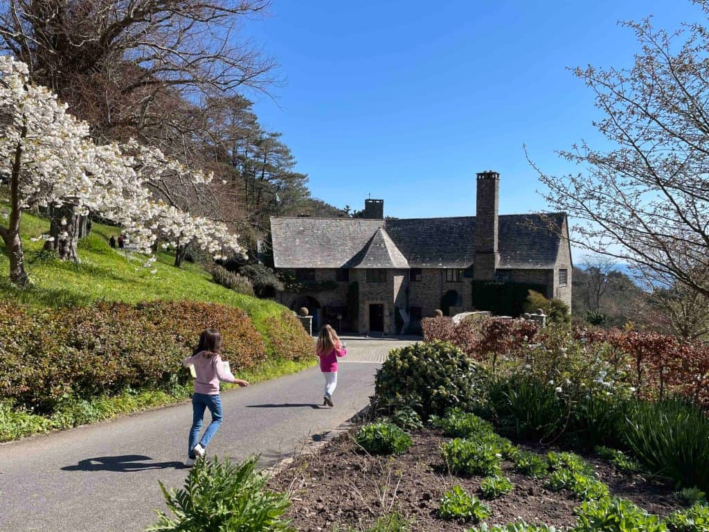 Children running down path towards Coleton Fishacre house with spring flowers to either side