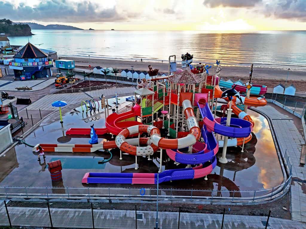 Shipwreck Island aqua park with brightly coloured tube slides and a tipping bucket at Splashdown Quaywest in Paignton. The sun is shining on the sea in the background