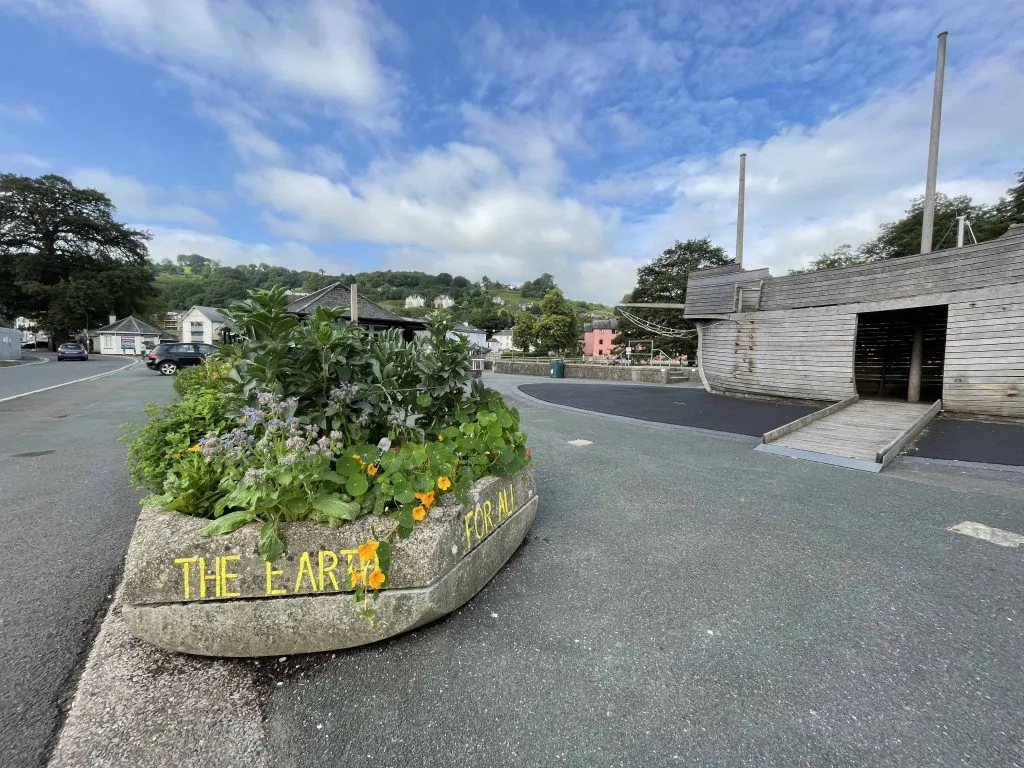 A raised flower bed in front of a children's play area shaped like a pirate ship