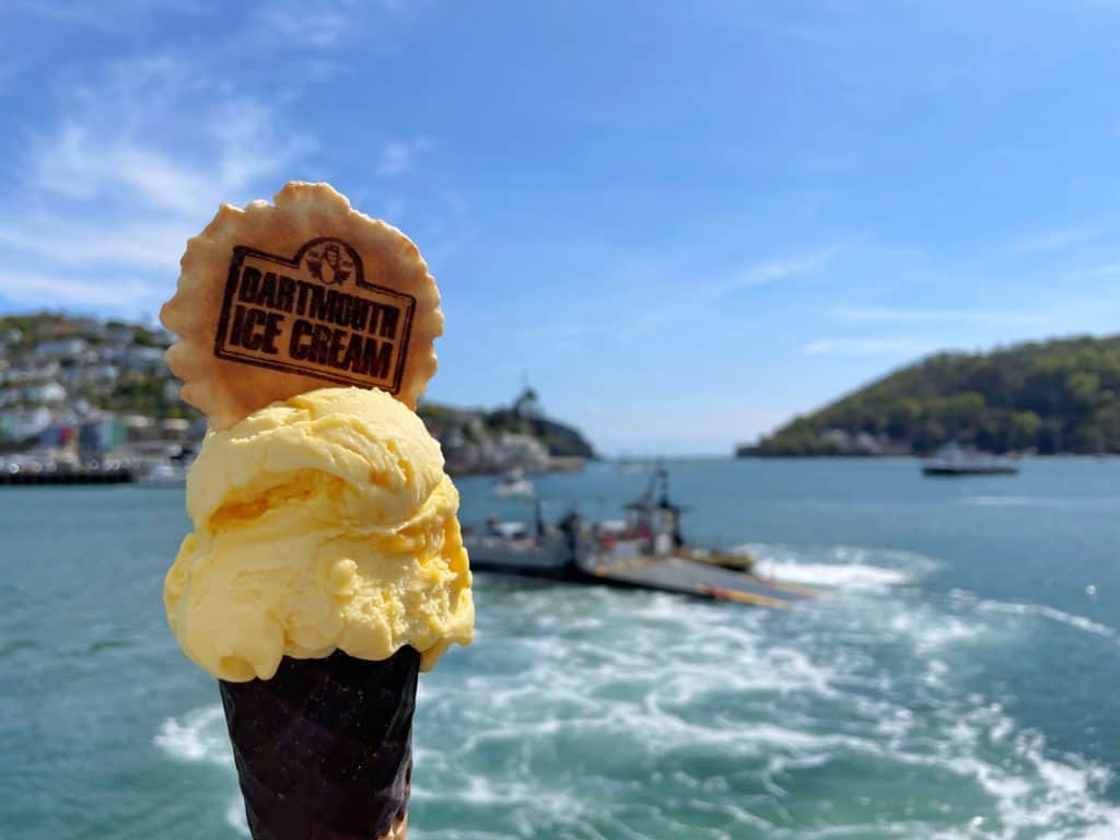 Cone of cream coloured ice cream with Dartmouth Ice Cream branded waffle flake in the top in front of a view of Dartmouth river