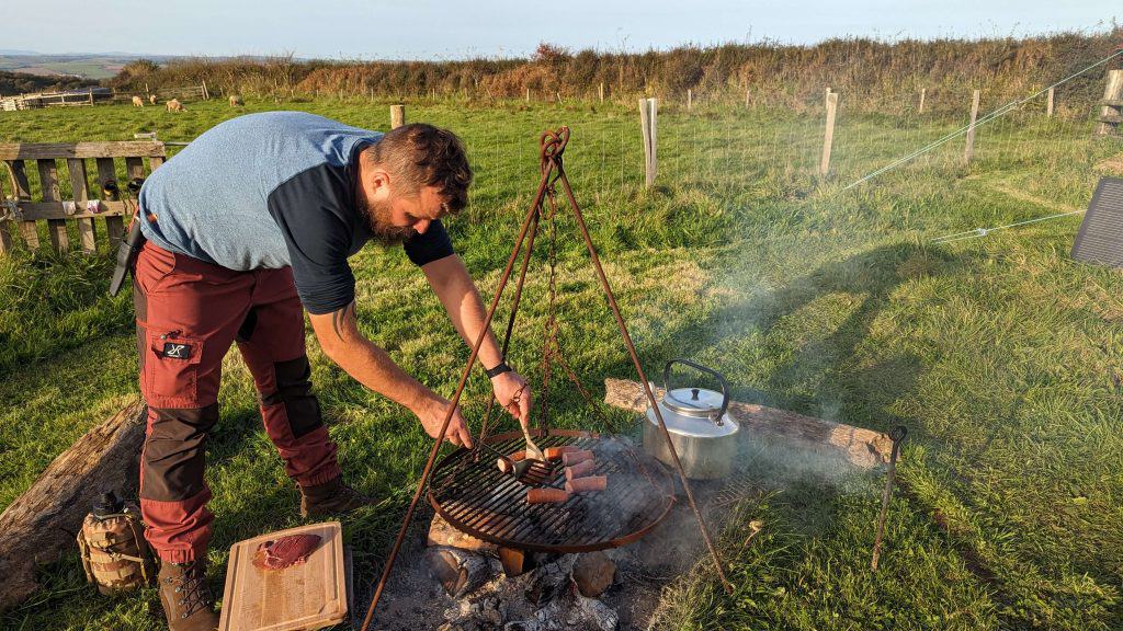 Stacey's husband cooking sausages on a gird above an open fire