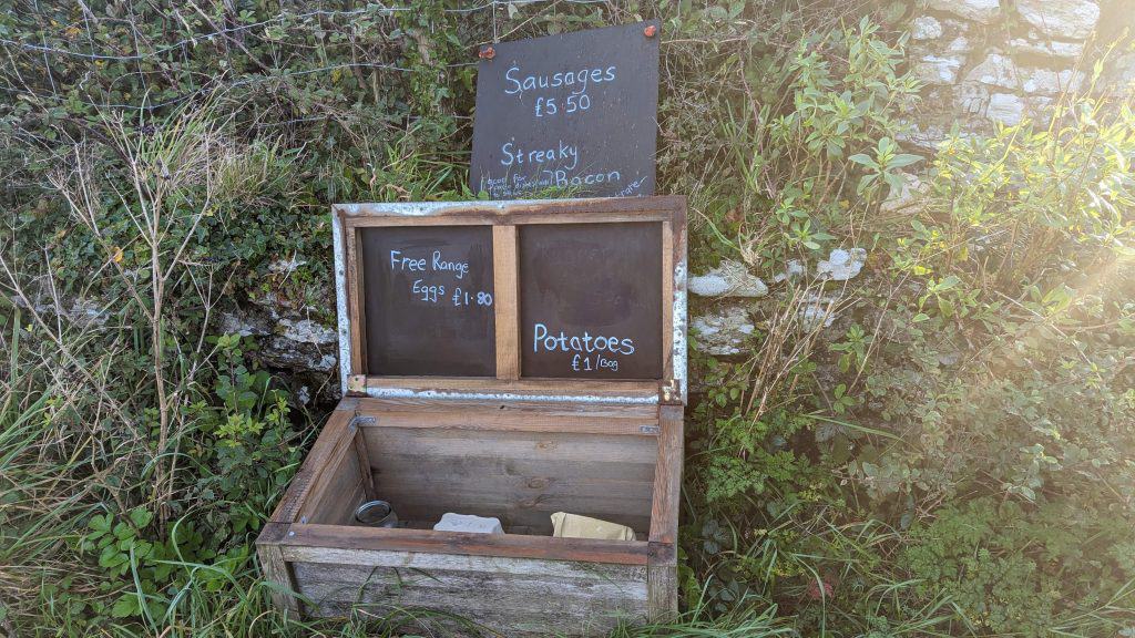 A small farm honesty box containing sausages and potatoes