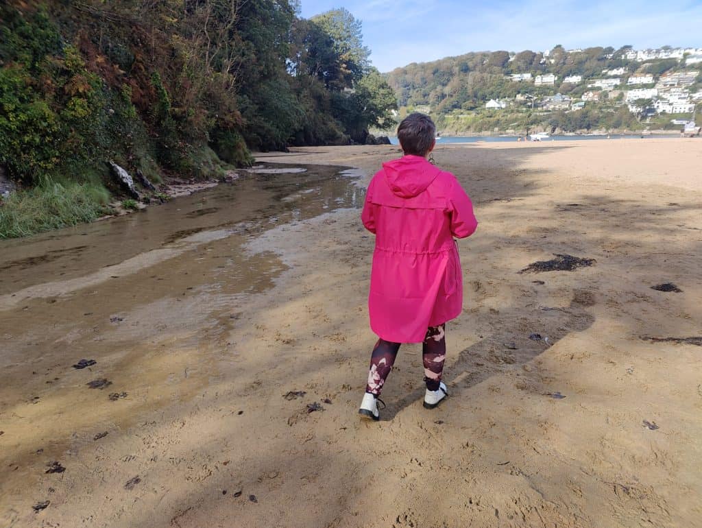 Stacey stood on the sand at Mill Bay beach wearing a bright pink coat