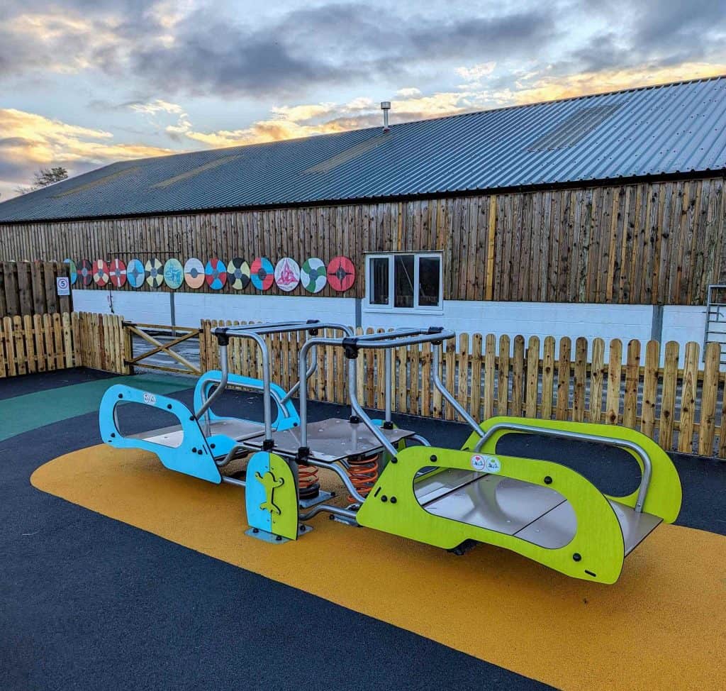 A colourful wheelchair accessible see saw in a playground at Made-Well CIC in Devon