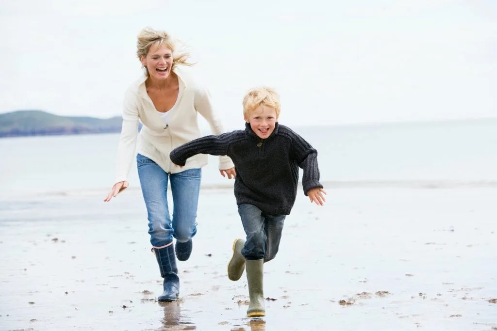 Mother and son running on beach. It's a spring day and they are wearing wellington boots