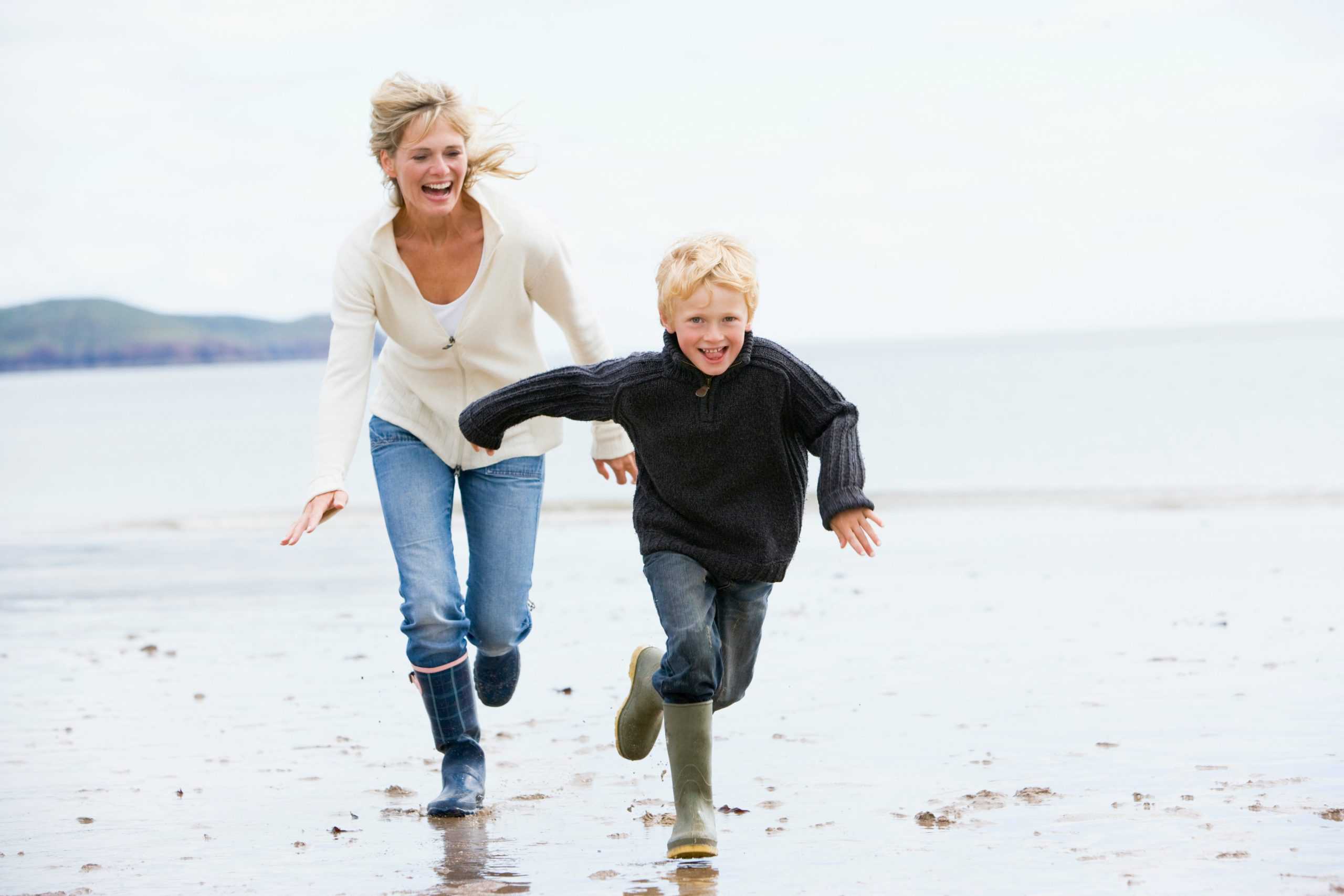 Mother and son running on beach. It's a spring day and they are wearing wellington boots