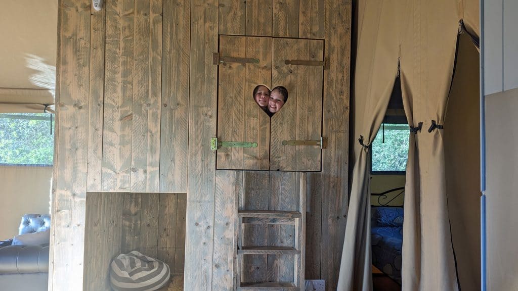Stacey's children peeping out of a heart shaped window in the cabin bed in a safari tent at Valleyside Escapes