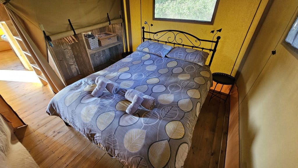 Iron frame double bed with blue patterned bed spread inside glamping tent