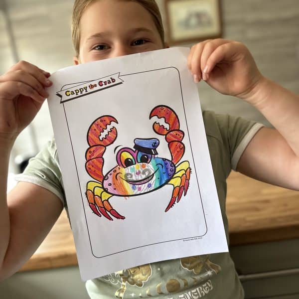 Child holding picture of Cappy the Crab character coloured in rainbow colours