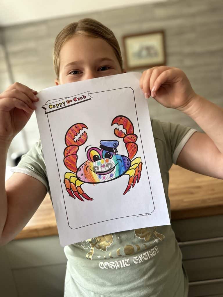 Child holding picture of Cappy the Crab character coloured in rainbow colours