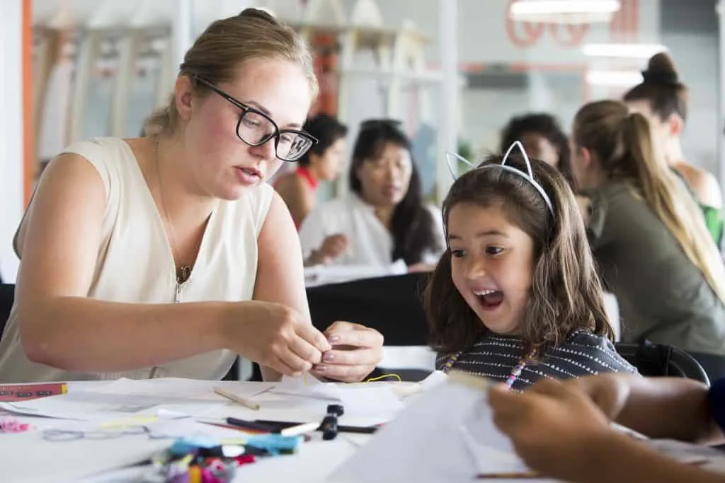 Child looks amazed as a young women shows are how to do something in a classroom setting