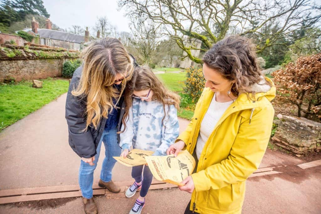 Family look at a treasure trail map outside Cockington Court