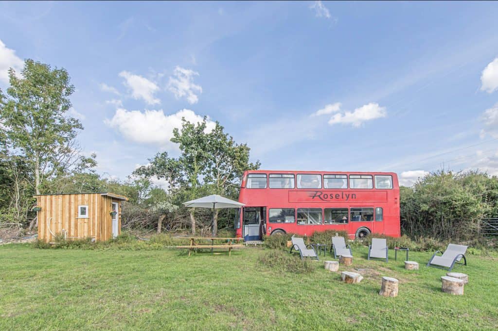 Red double decker bus converted into glamping accommodation in a field