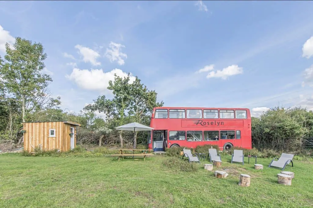 Red double decker bus converted into glamping accommodation in a field