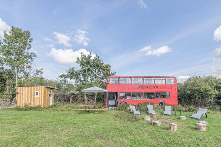 Red double decker bus converted into glamping accommodation in a field